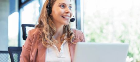 Frau am Laptop, die über ein Headset ein Gespräch führt.