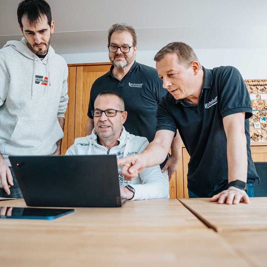 Vier Mitarbeitende von mIT solutions arbeiten gemeinsam am Laptop, besprechen Inhalte und optimieren digitale Prozesse im Team