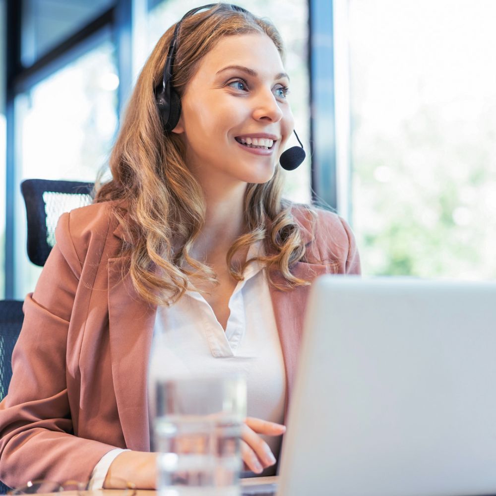 Frau am Laptop, die über ein Headset ein Gespräch führt.